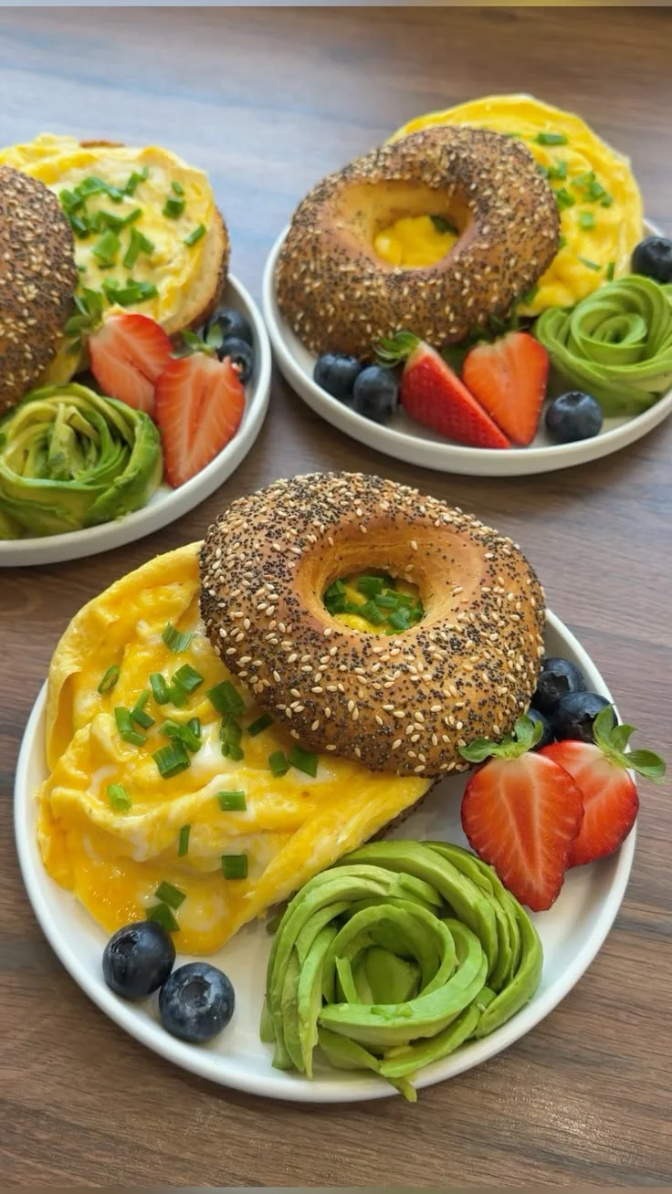 Desayuno antiinflamatorio con bagel, huevos revueltos, aguacate en rosa, fresas y arándanos